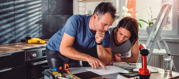 A contractor and homeowner reviewing plans in a kitchen or bathroom setting.
