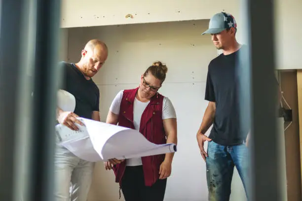 Contractor reviewing renovation plans with homeowners in a small bathroom under construction.