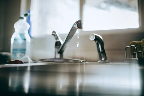 A water faucet with droplets and a home background, symbolizing water conservation in remodeling.