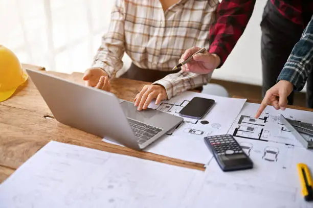 Homeowner and contractor reviewing a detailed remodeling estimate with blueprints and a laptop.