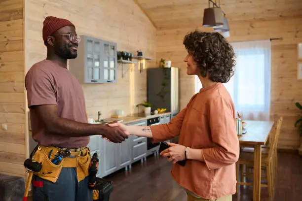 Contractor and homeowner shaking hands in a partially remodeled kitchen with tools nearby.