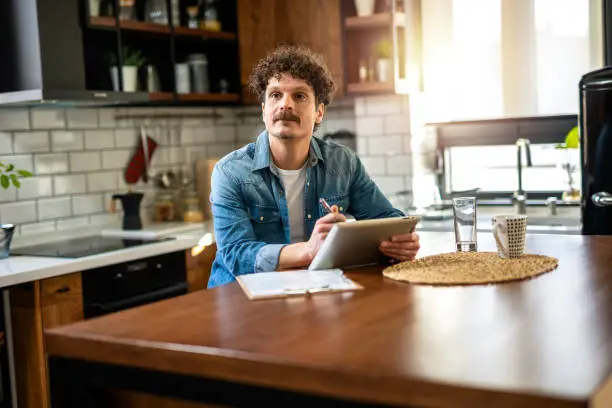 Homeowner planning a budget-friendly kitchen remodel with a checklist and digital tablet.
