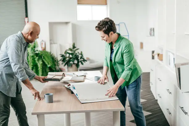 A contractor and homeowner reviewing eco-friendly material samples and biophilic design plans at a bright workspace.