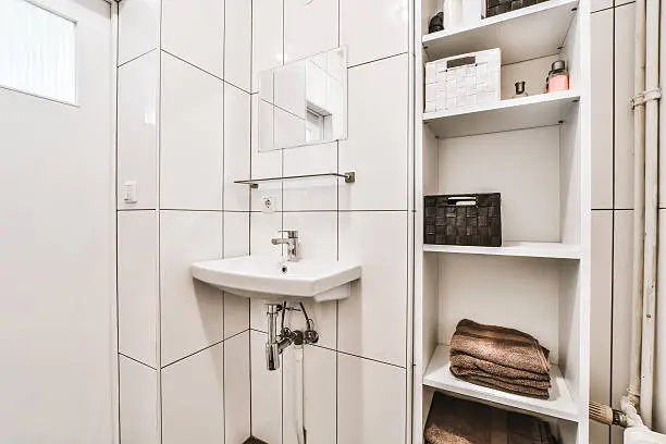 Compact bathroom with corner sink and vertical storage solutions for creative space use.