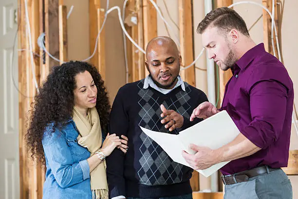 Homeowners consulting with a contractor while reviewing sustainable renovation plans.
